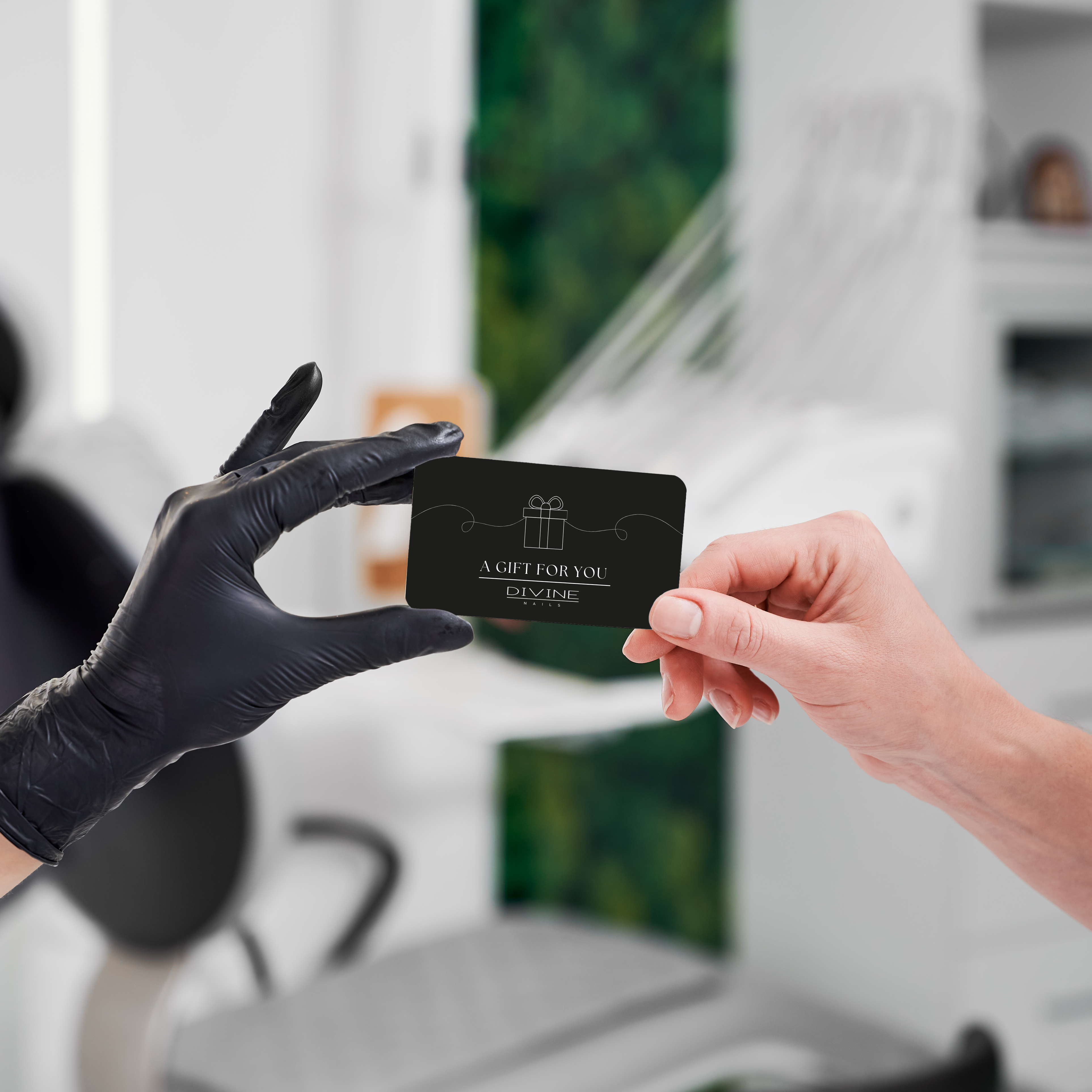 Divine Nails Red Deer - Gift Card 1 Tech with a glove passing a gift card to a client with a blured nail salon background.
